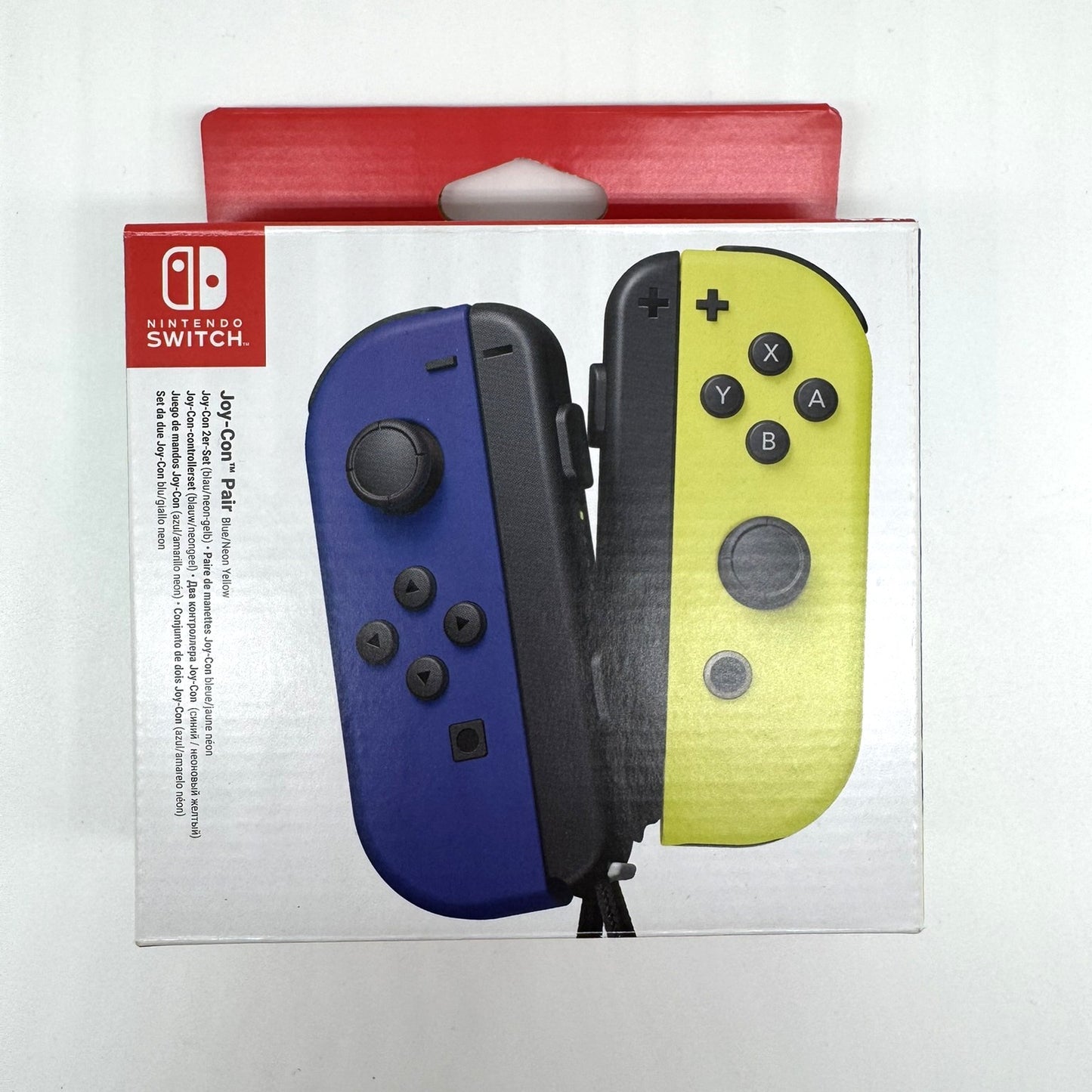 Verpackung eines Nintendo Switch Joy-Con Paars in den Farben Blau und Gelb. Das Design zeigt die Joy-Cons nebeneinander mit typischen Bedienelementen, auf weißer Verpackung mit rotem Kopf.