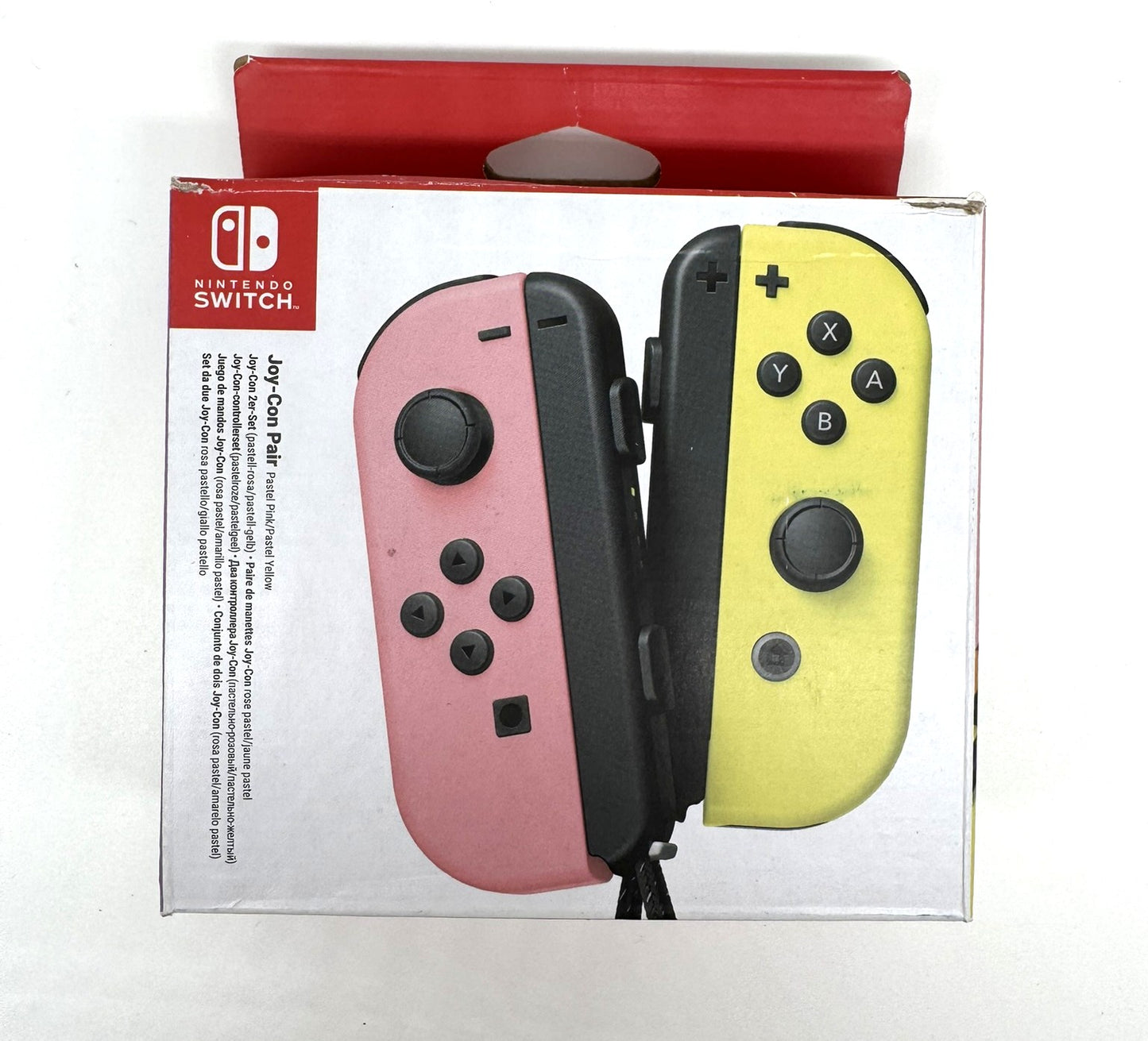 Verpackung eines Nintendo Switch Joy-Con Sets mit zwei unterschiedlich farbigen Controllern – links rosa, rechts gelb. Die Vorderseite zeigt die typische Nintendo-Verpackung mit weißer Fläche und rotem Griffbereich.