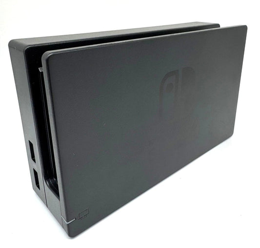 Das Bild zeigt die Nintendo Switch Dockingstation in einer leicht seitlichen Perspektive, wodurch die beiden seitlichen USB-Anschlüsse sowie der Einschubschlitz für die Konsole sichtbar sind. Das schwarze Gehäuse trägt das eingelassene Nintendo Switch Logo. Der weiße Hintergrund hebt das Produkt gut hervor und lässt die technischen Details und Anschlüsse gut erkennen. Die Darstellung eignet sich gut zur Produktbeschreibung.